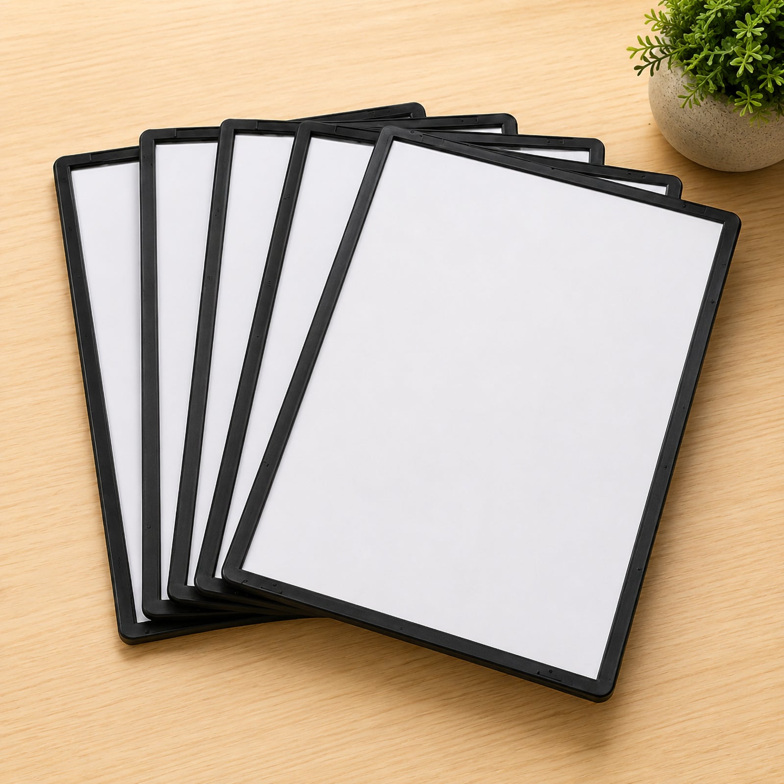 Five Durable Sherpa A4 black display panels are neatly fanned across a light timber desktop beside a small potted plant. The image showcases the pack quantity, slim profile and professional finish for office document organisation.