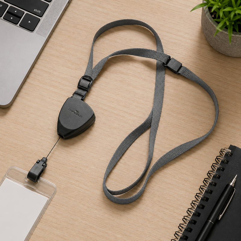 Top view of the Durable Textile Lanyard Flex arranged on a timber office desk beside a laptop, notebook, pen and indoor plant. The image showcases the retractable badge reel, adjustable textile strap and secure snap hook.