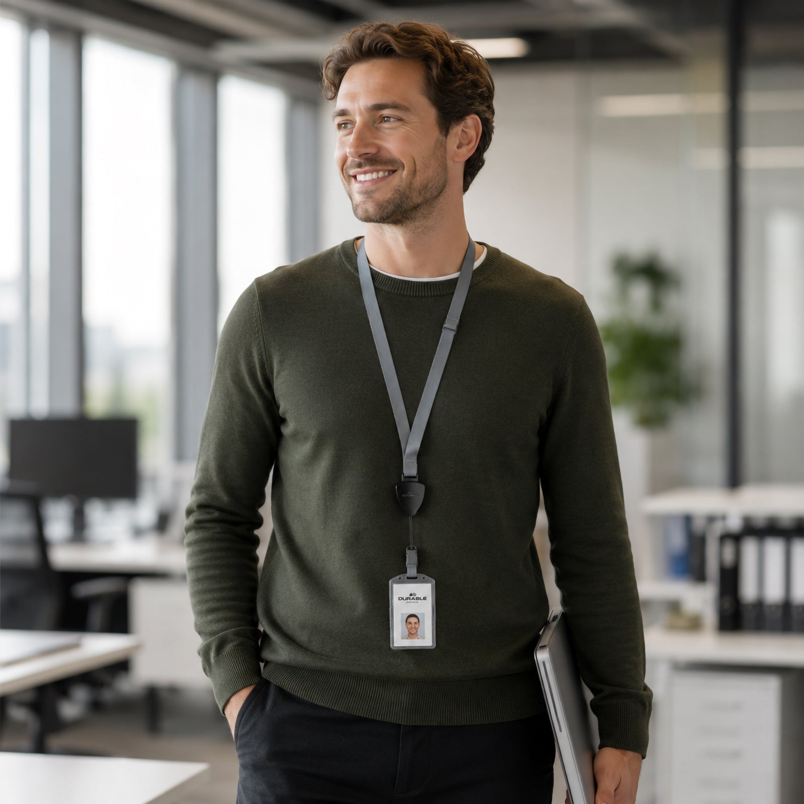 Professional employee walking through a modern office wearing the Durable Textile Lanyard Flex with retractable badge reel and identification card. The grey and black lanyard demonstrates comfortable all day wear and professional workplace identification.