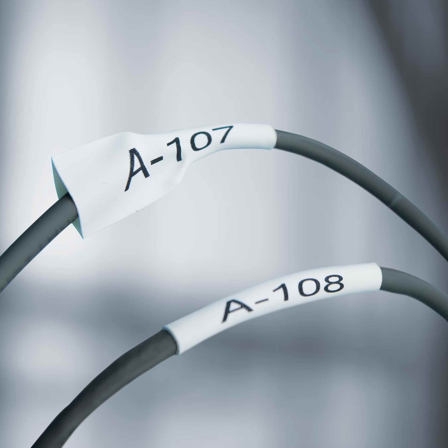 Two gray cables with labels 'A-107' and 'A-108' on a blurred gray background.