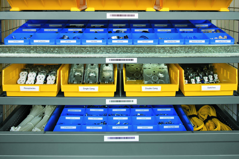 Warehouse shelving with yellow and blue parts bins, each shelf edge and bin carrying a printed white Dymo label.