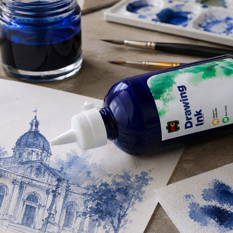 Close up view of Educational Colours Drawing Ink 500ml Cobalt positioned beside a detailed architectural artwork rendered in layered blue tones. Fine brushes, a glass ink container, palette and colour sample sit around the bottle, highlighting its use for precise illustration, tonal washes and creative experimentation.