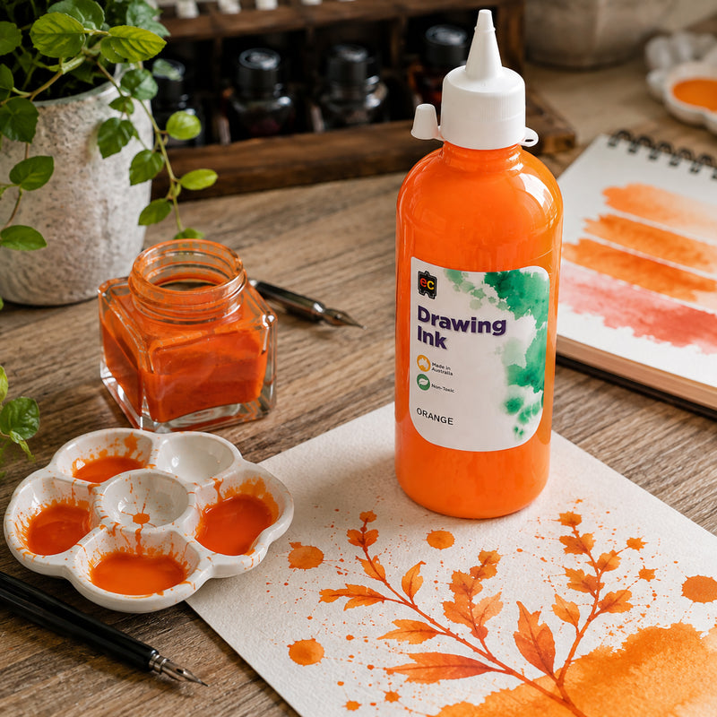 Educational Colours Drawing Ink 500ml Orange displayed upright in a bright creative workspace with an Orange botanical study, colour swatches, mixing palette and ink jar. The scene demonstrates the energetic colour for painted leaves, experimental washes and artistic mark making while keeping the product clearly visible.