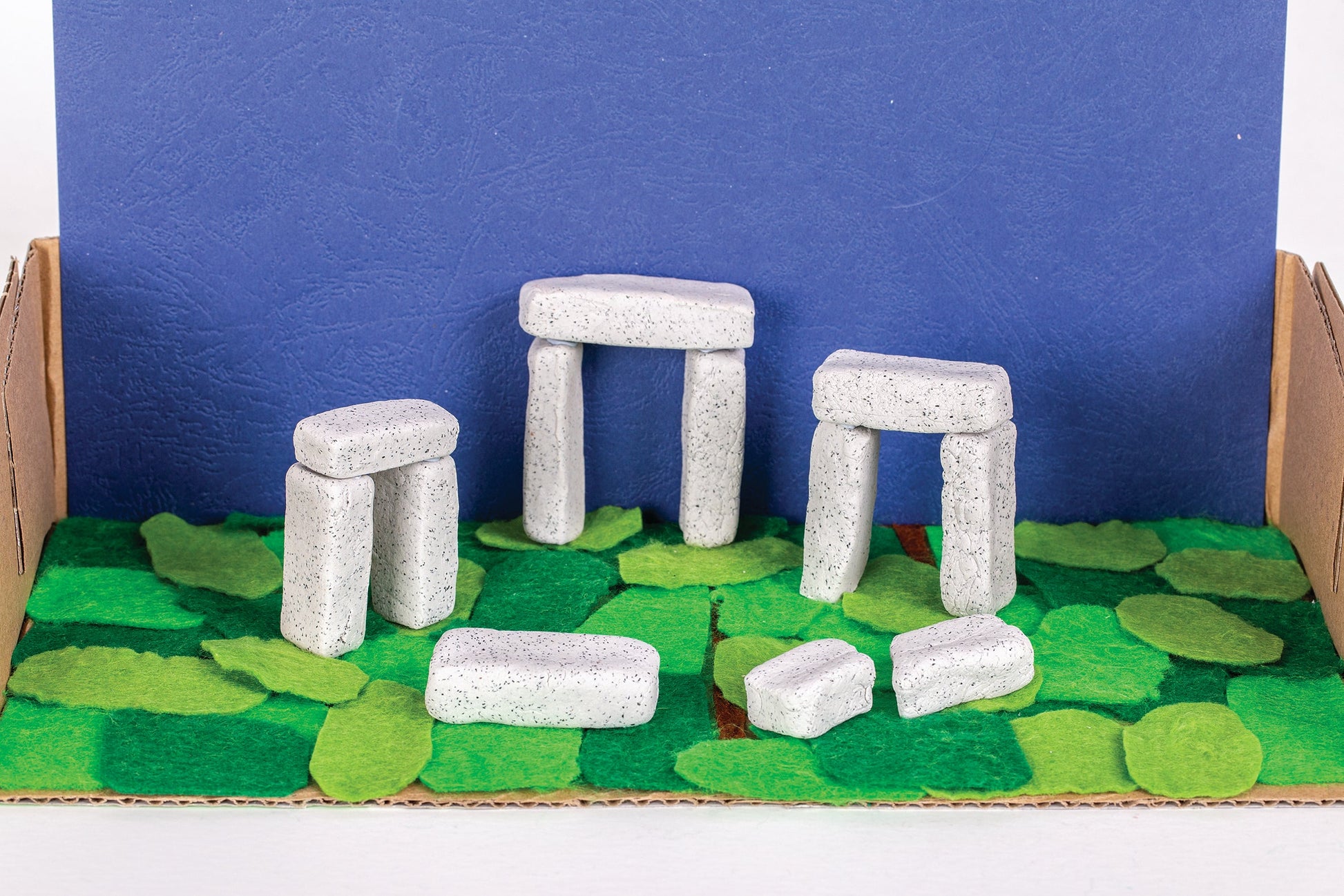 Several finished Rock Clay ornaments in natural stone grey arranged on a classroom table alongside the open tub.