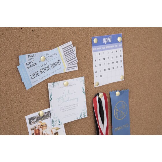 Brass drawing pins holding concert tickets, a calendar, an invitation, a photo and a ribbon on a cork board