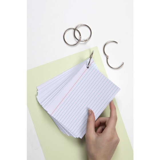 Hand holding a stack of white ruled index cards joined by a silver hinged ring, spare rings above