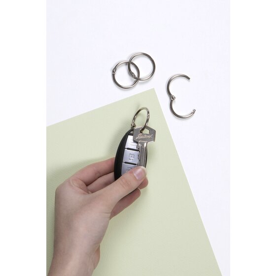 Hand holding a car key and black remote on a silver hinged ring, spare rings above