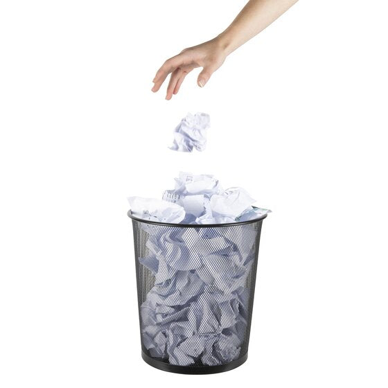 A hand dropping a crumpled paper ball into an Esselte black mesh waste bin already filled with screwed up paper