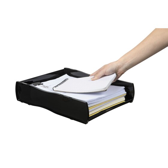 A hand placing a spiral notebook onto a stack of paper inside the black Nouveau document tray
