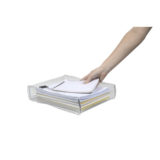 A hand placing a notebook on a paper stack in the clear Nouveau tray, with the paper visible through the sides