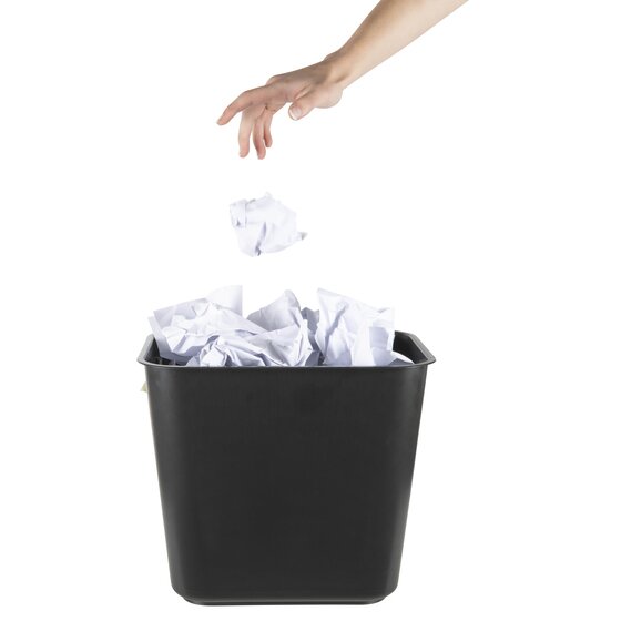A hand dropping crumpled paper into an Esselte SWS black square plastic waste bin that is already holding screwed up paper