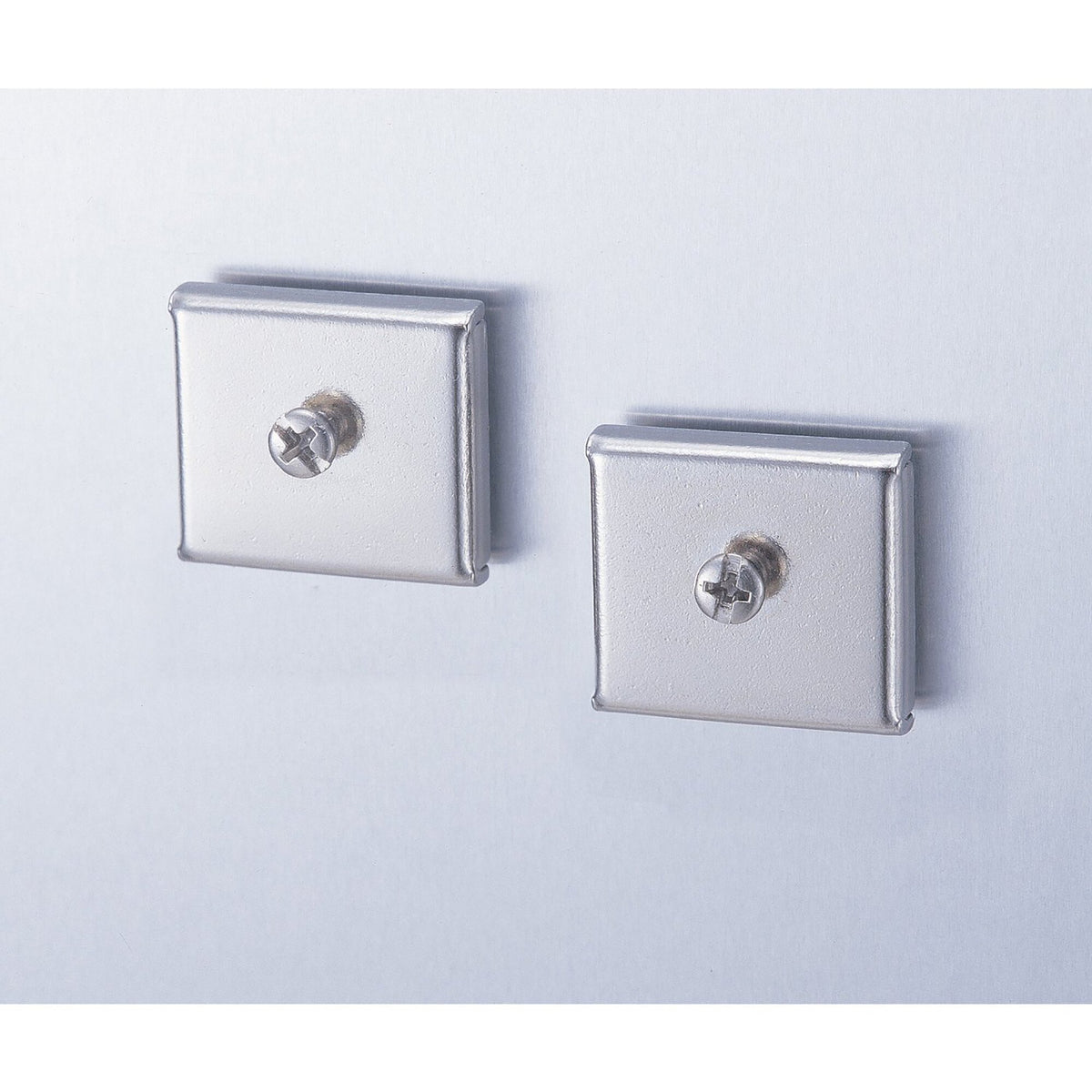 Two square brushed silver Esselte Verticalmate magnetic pads, each with a round headed screw stud in the centre, on a pale grey surface