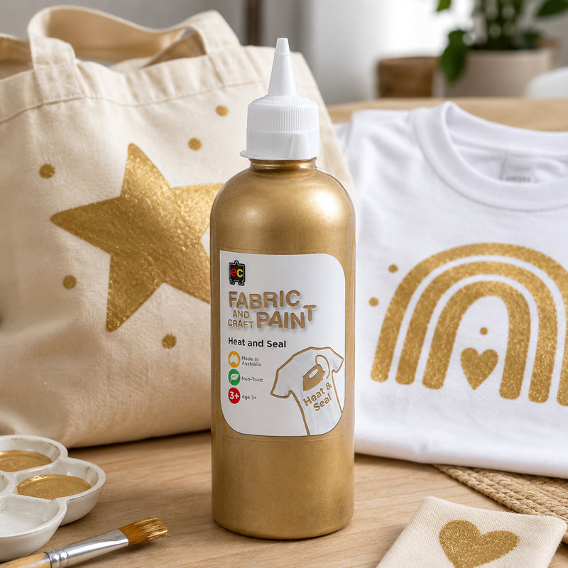 Educational Colours gold fabric paint shown beside a decorated tote bag and white shirt featuring bright metallic gold painted shapes and patterns in a creative studio setting.