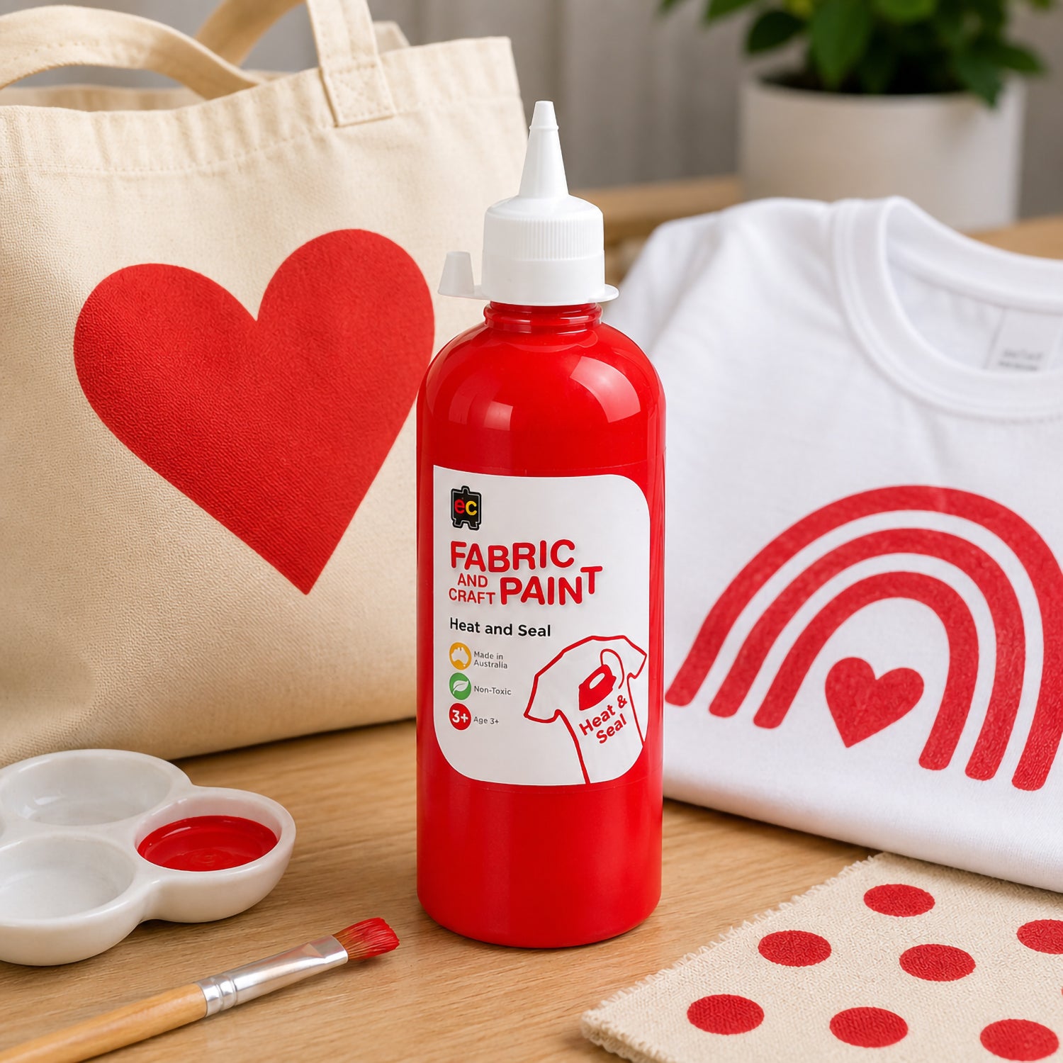 Educational Colours red fabric and craft paint shown beside a canvas tote bag and white shirt decorated with bold red heart and rainbow themed fabric artwork.