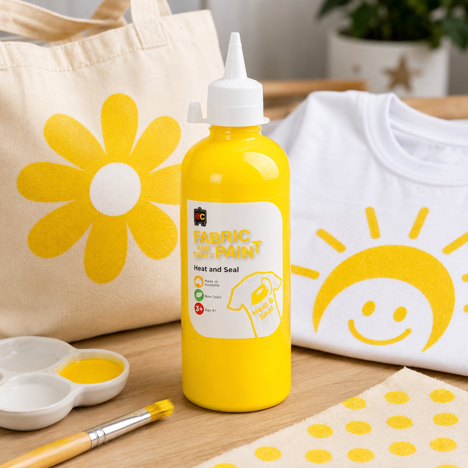 Educational Colours yellow fabric paint featured with a painted tote bag and white shirt decorated with cheerful yellow flower and sunshine artwork in a creative home studio environment.