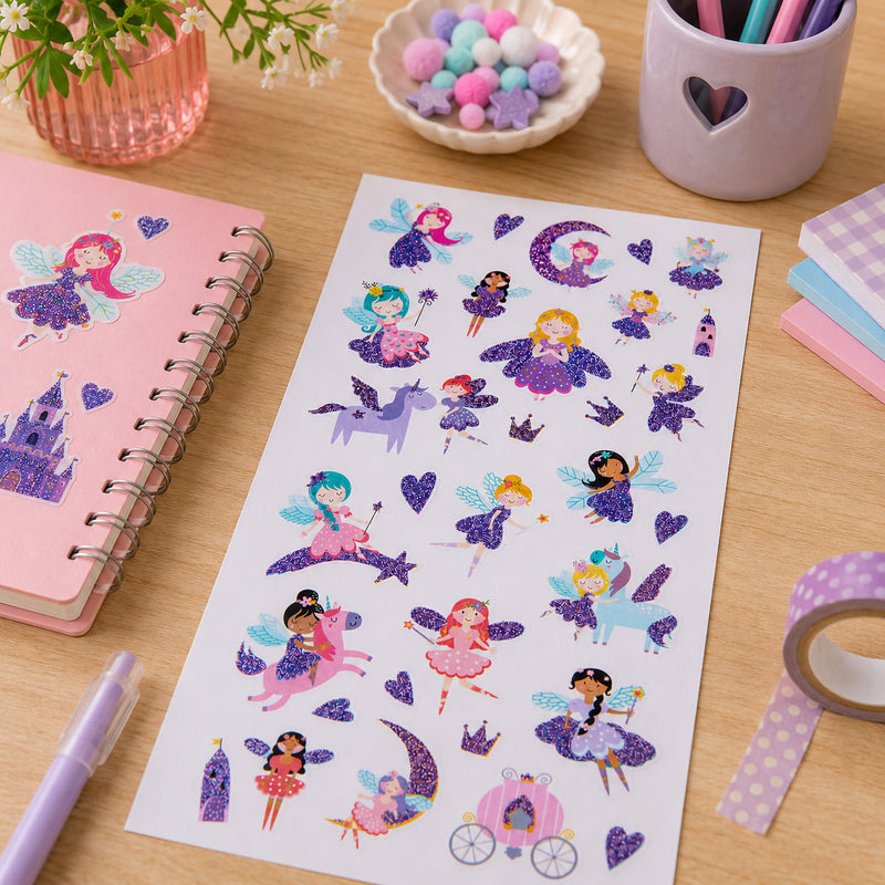 Sticker sheet arranged with stationery, decorative pom poms and colourful pens. The magical assortment showcases fairy characters with shimmering wings and sparkling fantasy accessories.
