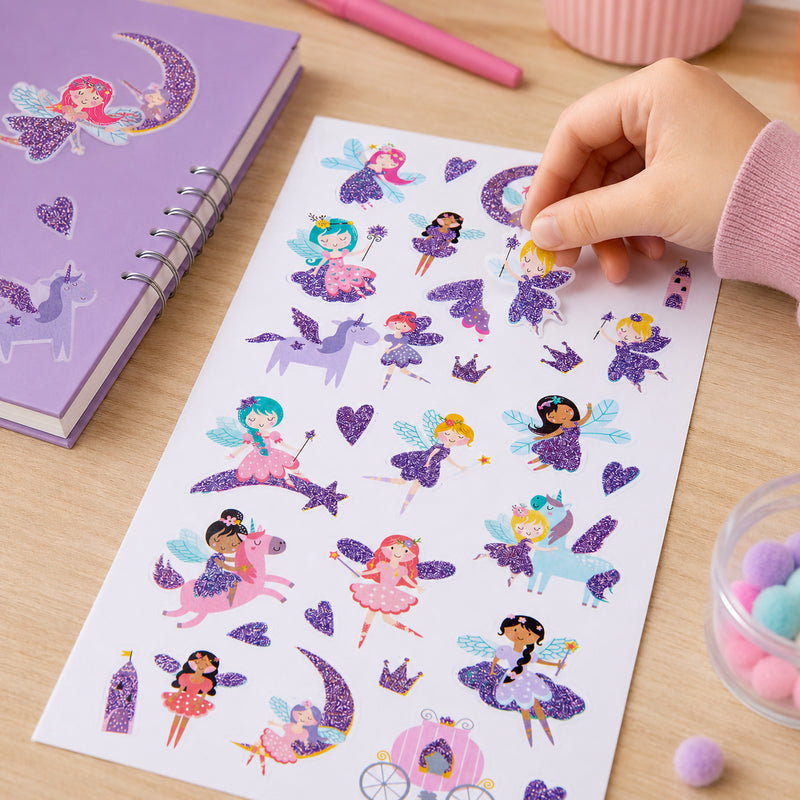Child placing a glitter fairy sticker onto a craft project while surrounded by colourful fantasy themed stickers. The sheet features sparkling fairies, unicorns, hearts and magical fairy tale designs in soft pastel colours.
