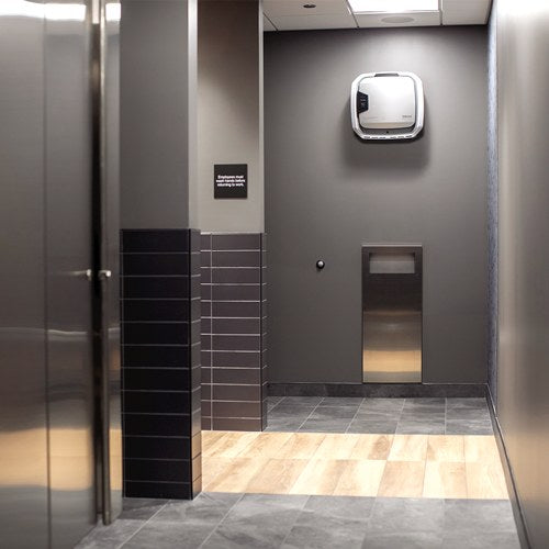 Grey tiled restroom corridor with an AM 3 PC purifier mounted high on the wall above a paper towel dispenser