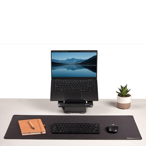 Black Breyta desk mat under a keyboard, mouse and orange notebook, with a laptop on a stand and a pot plant behind