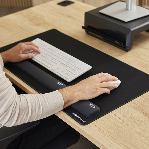 Hands typing on a white keyboard and using a mouse on a black Breyta desk mat, with Breyta wrist rests and a monitor riser