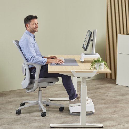 Man at a white sit-stand desk with a grey Breyta desk mat and a footrest under his feet