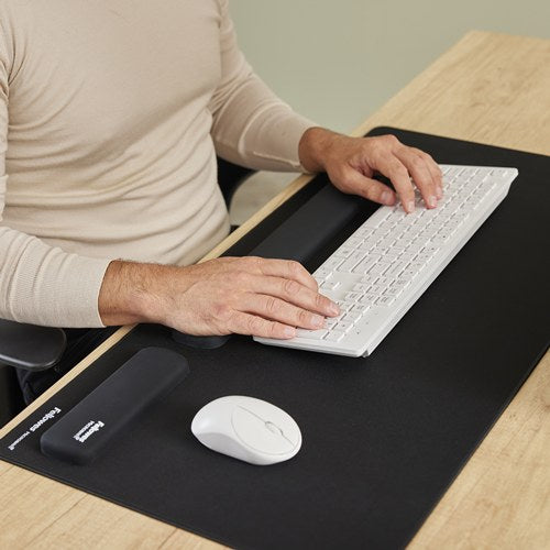 Hands typing on a white keyboard with wrists on the black Breyta rest, on a black desk mat beside a mouse and palm rest