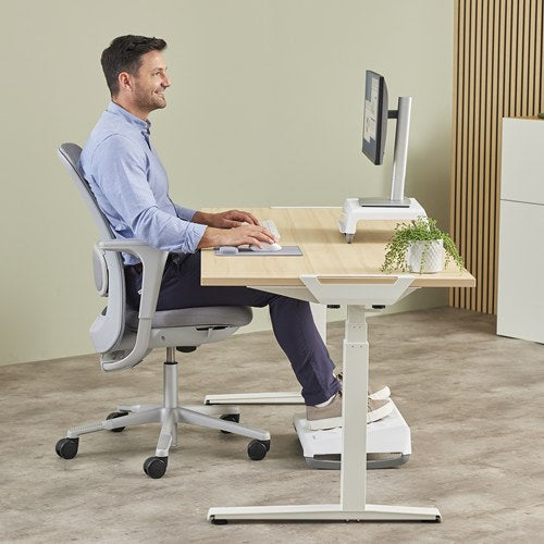 Man in a blue shirt at a sit-stand desk with the grey Breyta wrist rest in front of a white keyboard
