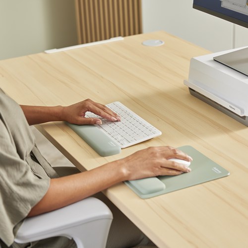 Hand on a white mouse on a Sage Breyta pad next to a Sage keyboard rest on a light timber desk