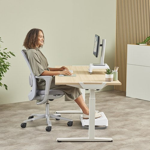 Woman at a sit-stand desk using a Sage Breyta mouse pad with a footrest under the desk