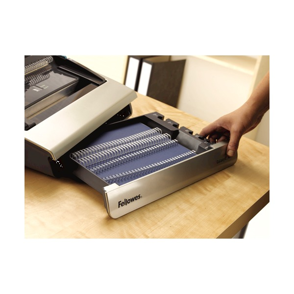 Hand pulling out the front storage tray of the Galaxy-E 130, filled with white wire combs, on a wooden desk
