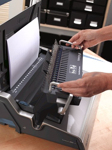 Two hands lifting the removable Satellite binding unit off the Galaxy-E base next to a stack of paper