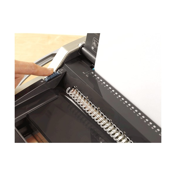 Finger pressing the closure control on the Galaxy wire binder beside a white wire comb held in the closing jaws