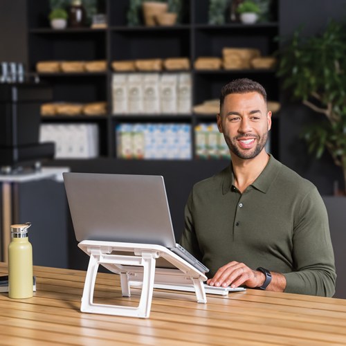 Smiling man in a cafe with his laptop raised on a white I-Spire Quick Lift and a separate keyboard in front