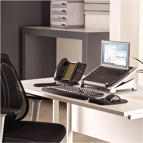 Office desk with a laptop on an Office Suites riser beside a phone, keyboard and mouse