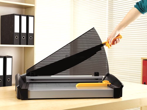Fellowes Plasma guillotine on an office desk beside binders, a hand bringing the cutting arm down