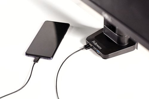 Phone charging from a USB port on the base of a Fellowes Platinum monitor arm under a black screen