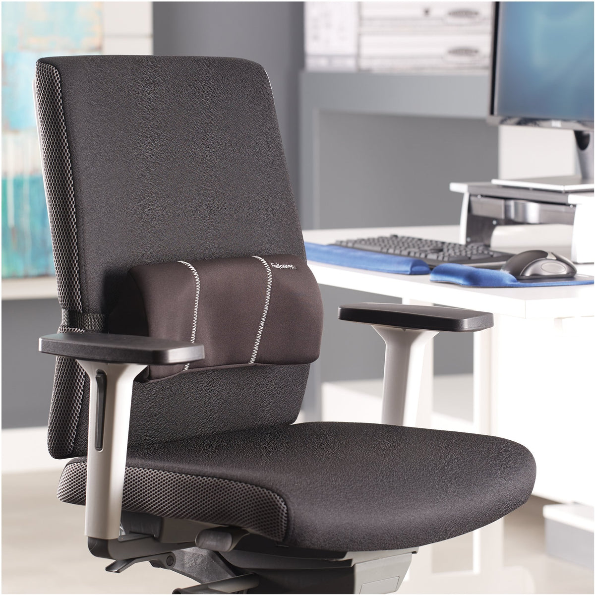 Office chair at a desk with the black Fellowes lumbar cushion fitted low on the backrest, in a bright office setting