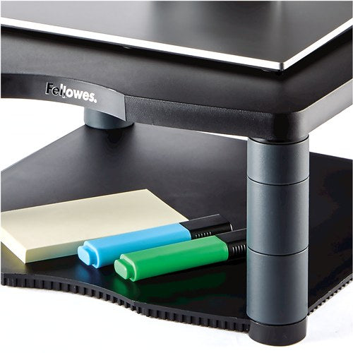Close-up of the lower shelf of the premium monitor riser holding sticky notes and two highlighter pens