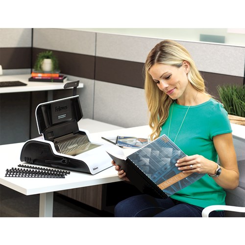 Woman seated at a desk reading a comb bound report with clear cover, a Pulsar+ 300 and loose combs beside her