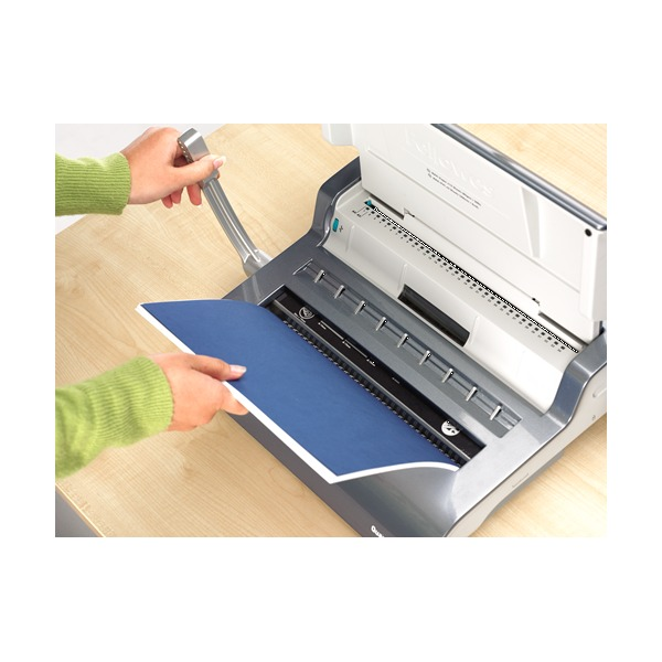Two hands working the Quasar 130 on a desk, one pulling the handle while the other holds a blue cover in the punch