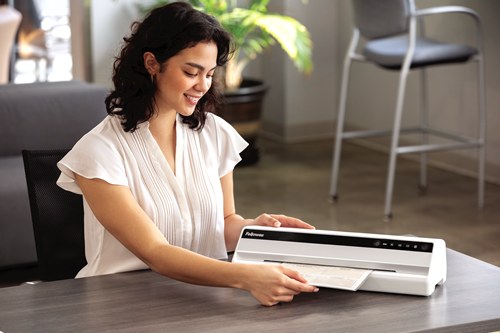Woman at an office desk feeding a pouch into a white Fellowes Saturn A3 laminator