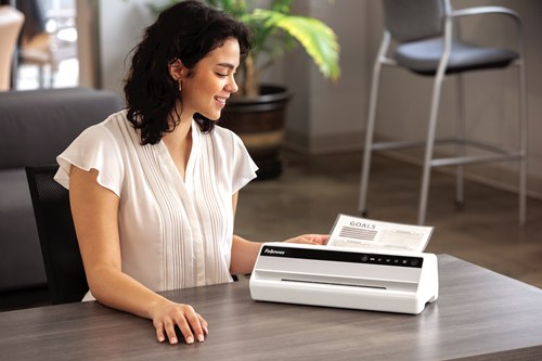 Woman at a desk beside a Fellowes Saturn A4 laminator as a laminated document comes out of the back
