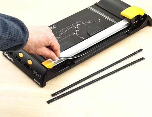 Hand fitting a new cutting strip into the base of a Fellowes rotary trimmer with two spare strips on the desk