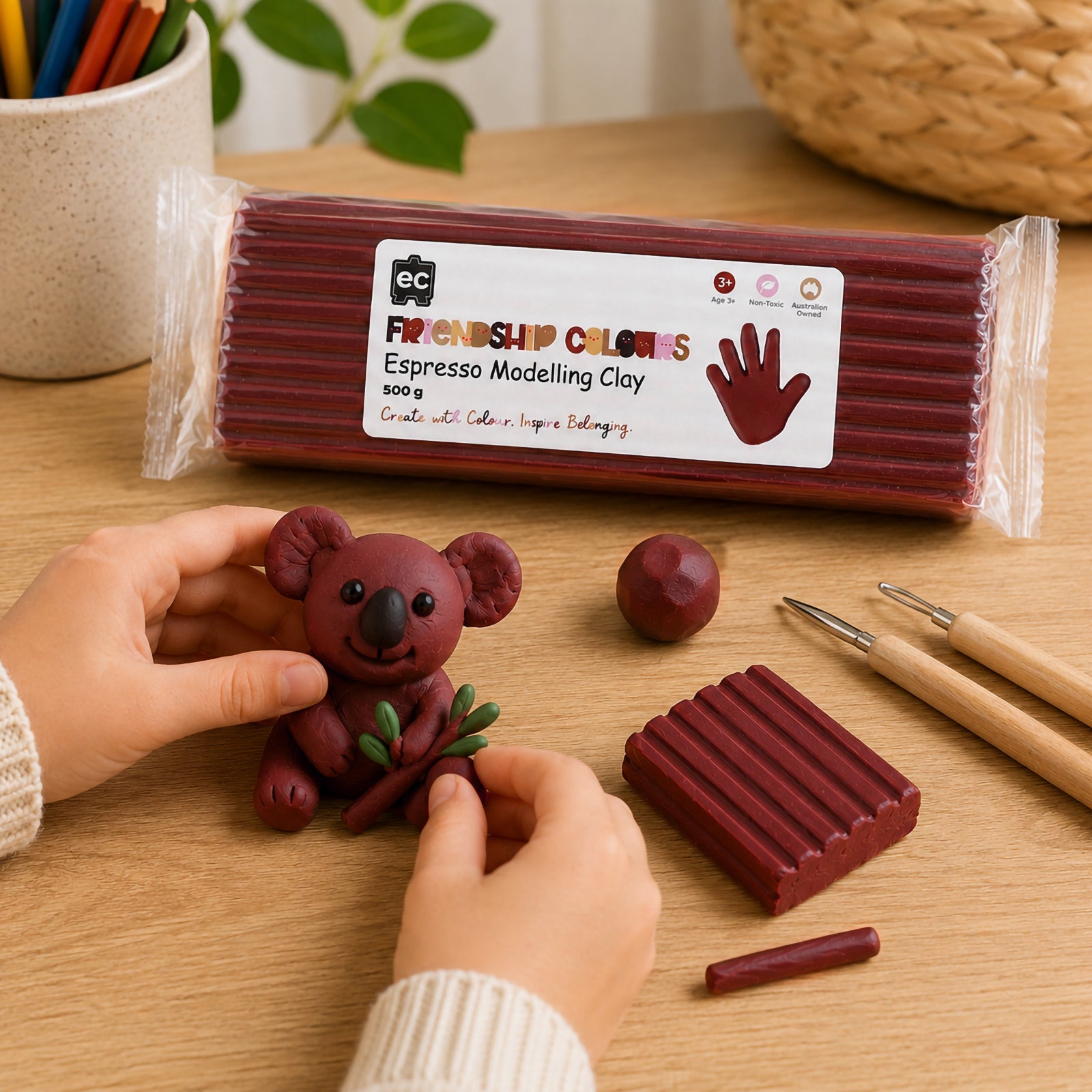 Child carefully positioning details onto a handcrafted koala model made from espresso coloured modelling clay. Sculpting tools, clay pieces and the packaged product are visible, illustrating hands on creative development, fine motor skill building and imaginative modelling activities.