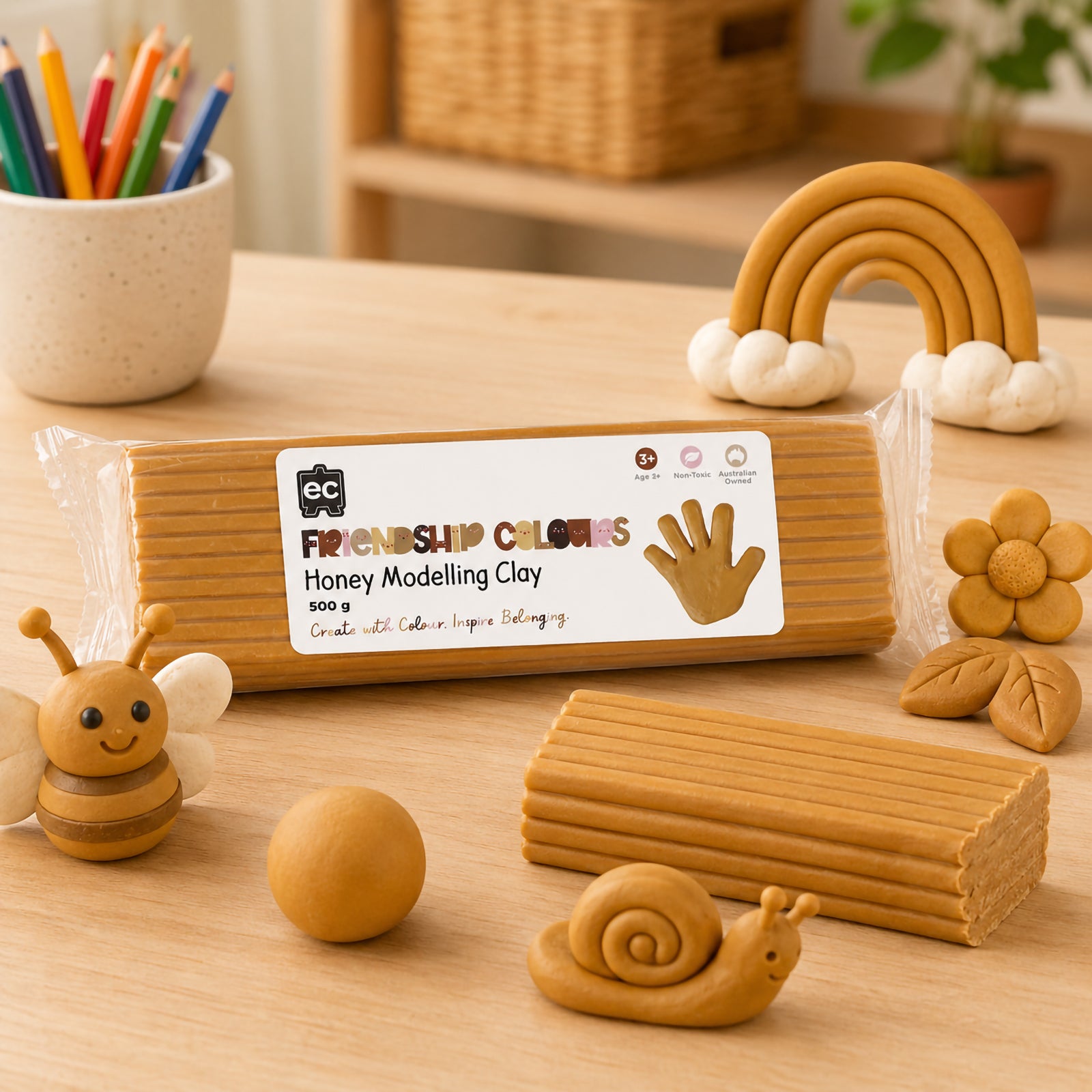 Honey modelling clay block presented alongside creative clay figures including a bee, rainbow, flower and snail. The image highlights the clay's soft, mouldable consistency and suitability for detailed classroom art activities and multicultural learning projects.