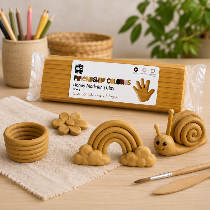 Educational Colours Friendship Colours Honey Modelling Clay 500g displayed with handcrafted clay creations including a rainbow, flower, bowl and smiling snail. The warm honey coloured clay showcases its smooth texture and versatility for inclusive art projects, sensory learning activities and imaginative sculpting experiences.