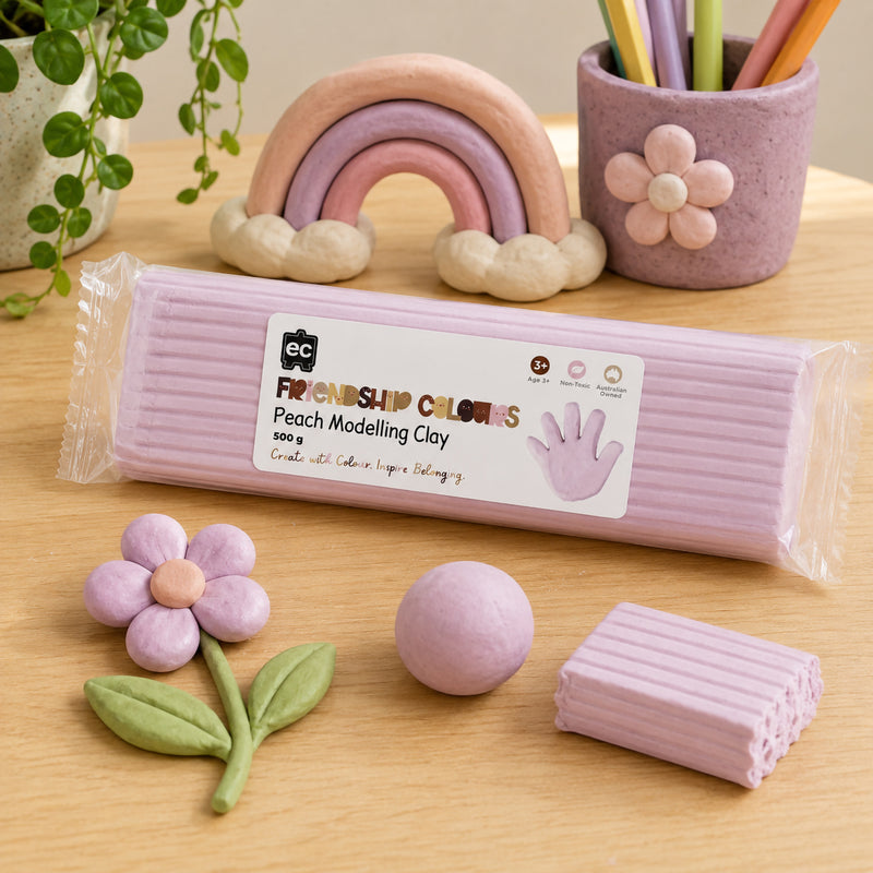 Friendship Colours Peach Modelling Clay 500g surrounded by pastel themed clay creations including a flower, rainbow and decorative pencil holder. The display demonstrates the clay's versatility for detailed sculpting, educational projects and creative storytelling activities.