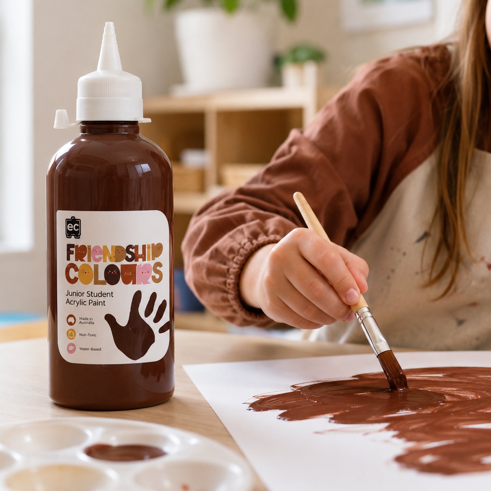 Friendship Colours Espresso Acrylic Paint 500ml featured alongside a young artist actively painting. The deep skin tone inspired colour demonstrates smooth coverage and is ideal for self portraits, multicultural artwork and educational creative projects.