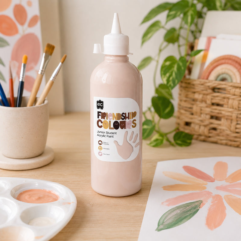 Educational Colours Friendship Colours Peach Acrylic Paint 500ml displayed beside a painted floral artwork, artist palette and classroom brushes. The soft peach skin tone paint is showcased in a welcoming creative environment that highlights inclusive art activities, self expression and multicultural learning experiences.