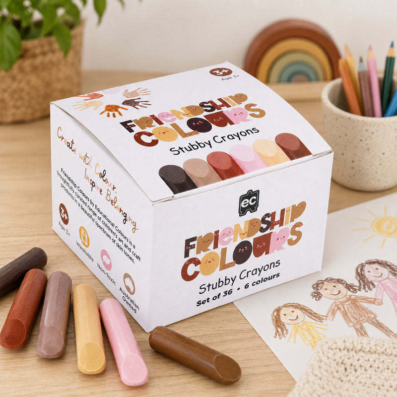 The Friendship Colours Stubby Crayons retail box is displayed alongside several crayons in different skin tone shades. Family themed drawings and educational surroundings highlight the crayons' focus on diversity, creativity and belonging.
